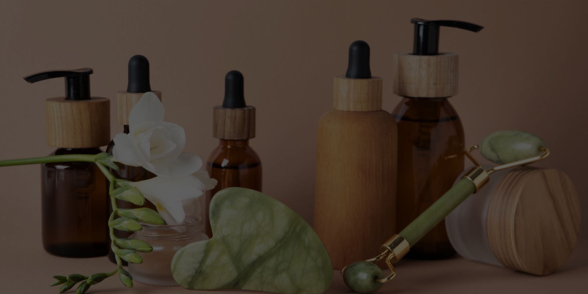 Collection of brown skincare bottles with green leaves and a bamboo tool on a brown background