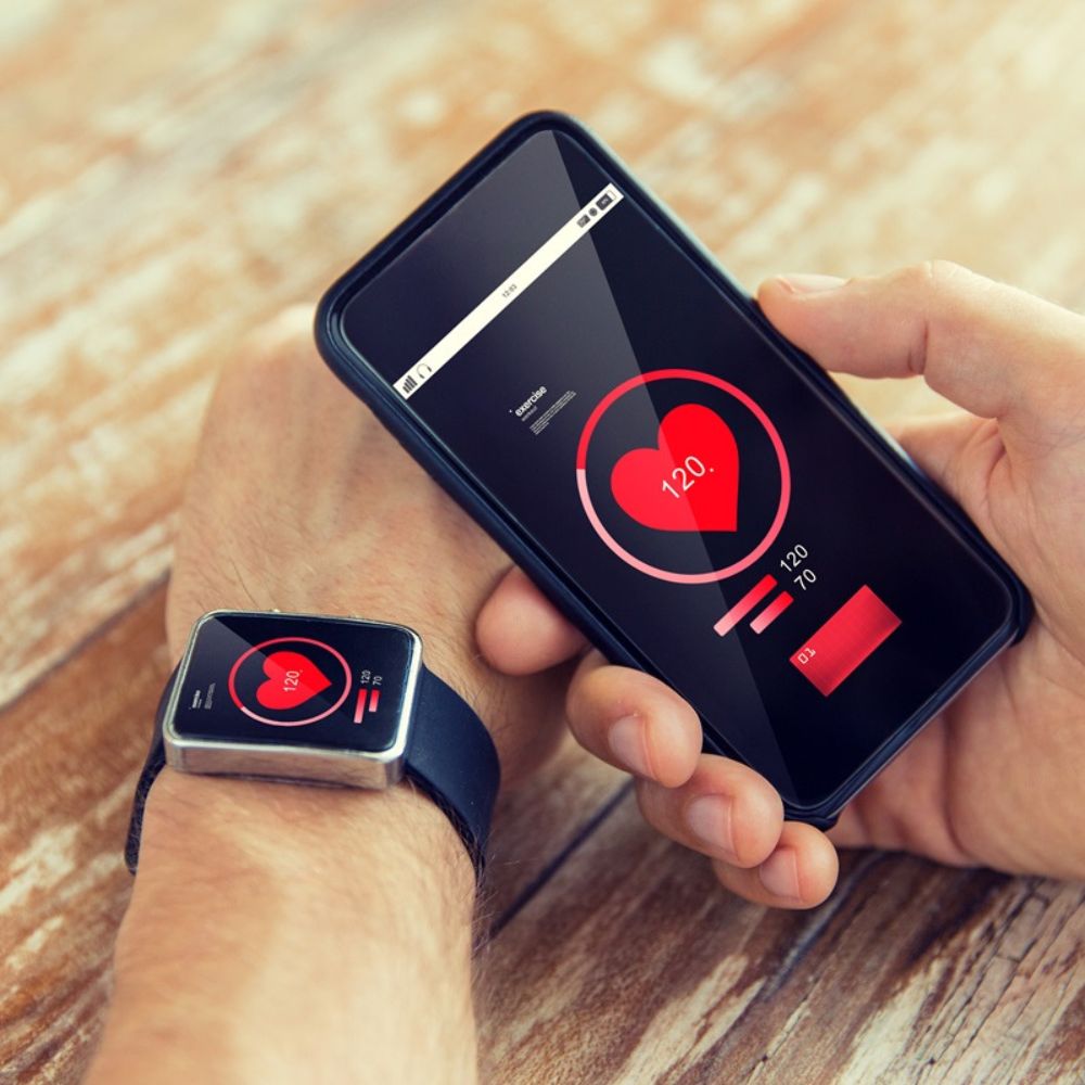 Smartwatch and phone displaying heart rate app on a wooden surface