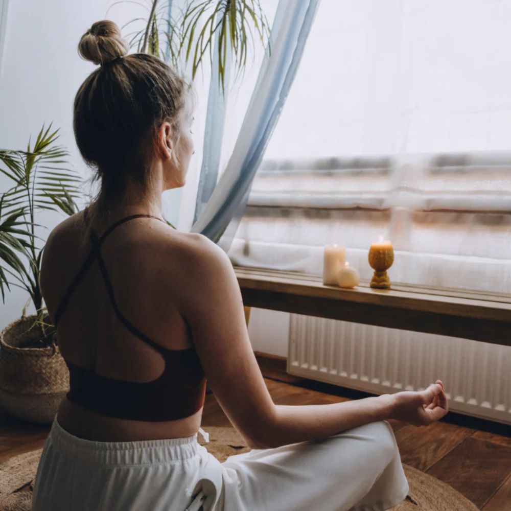Woman meditating by a window with candles and plants